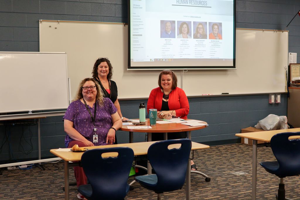 three women smile for the camera in a classroom