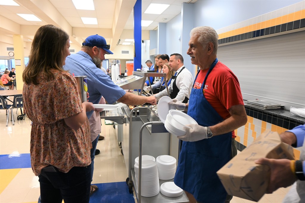 USD 503 Board member Lou Martino hands out plates to staff as they enter the line to get breakfast.