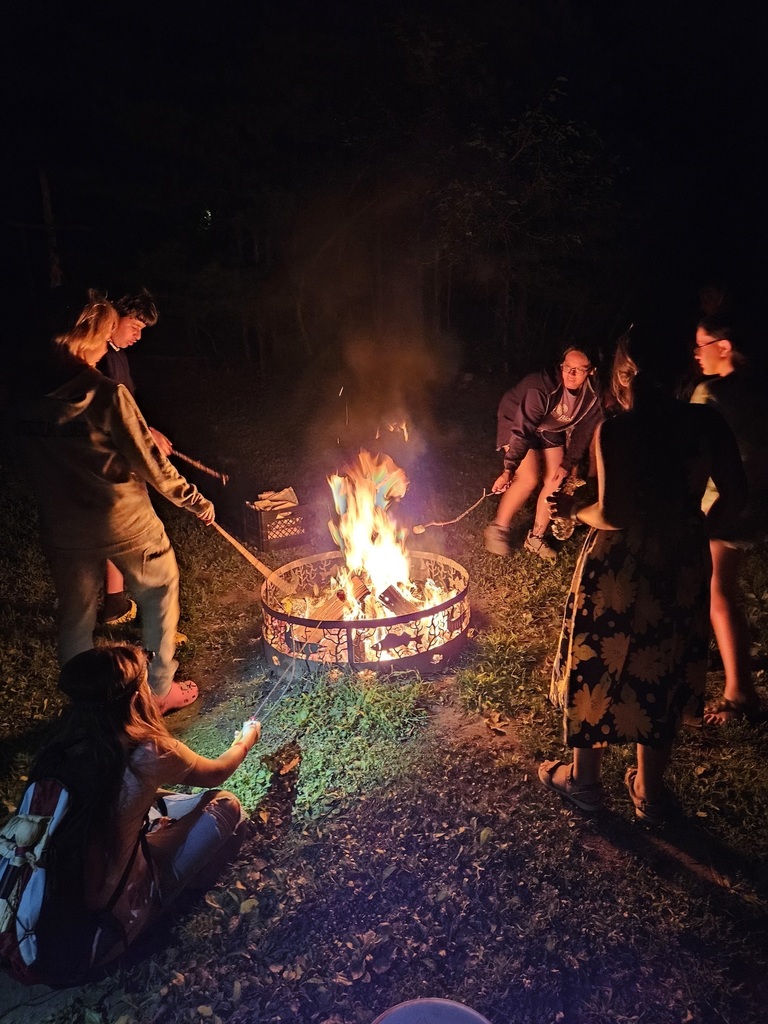 Family roasting marshmellows around the fire outside at night.