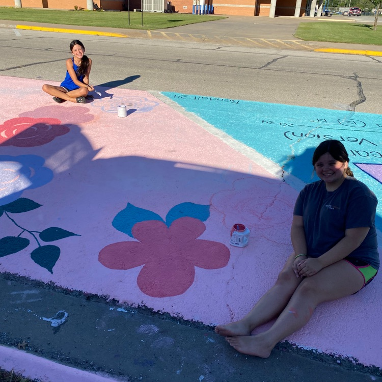 Two girls paint flowers on a parking spot at PHS. 