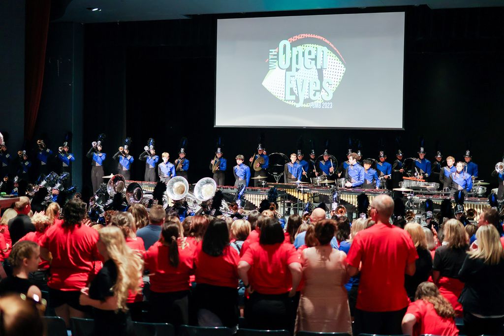 staff in an auditorium with a marching band on stage