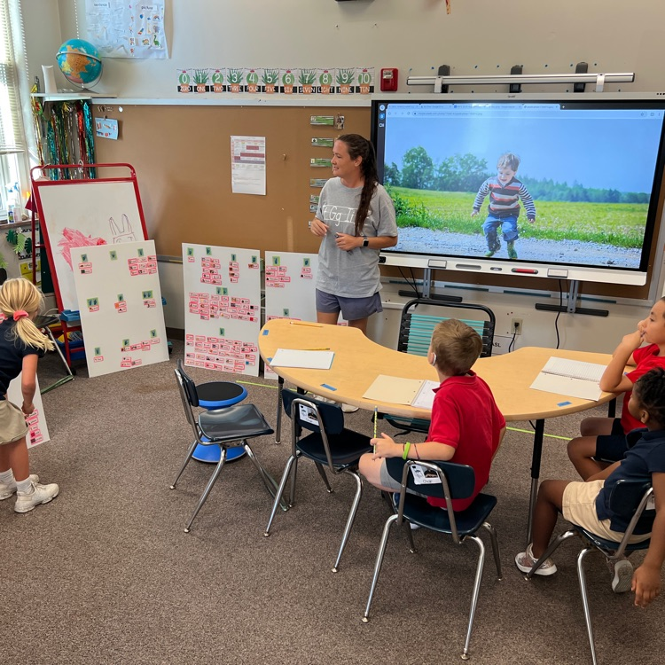 woman in a grey shirt interacts with a female student in a blue shirt in a classroom setting