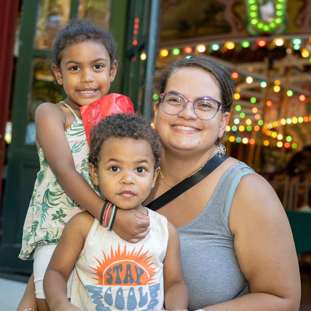 A mother and her children posing for a picture in front of the Holyoke Merry Go Round. 