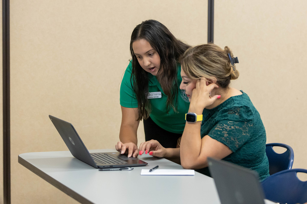 Staff member in green shirt working with parent at computer