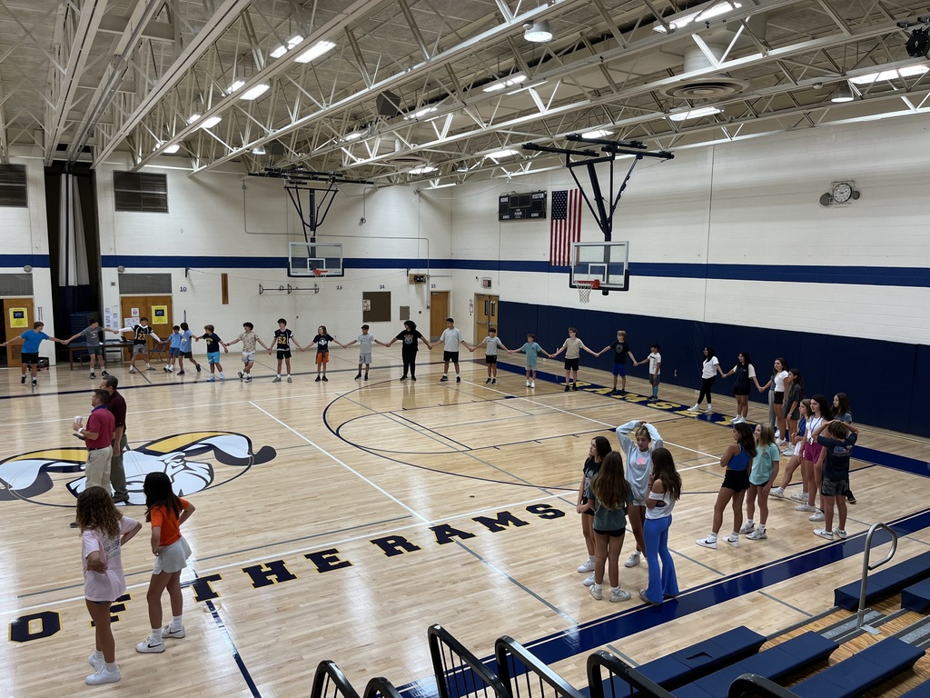 8th grade students participating in a team building activity of passing a hula hoop through their entire team around the gym without breaking hands