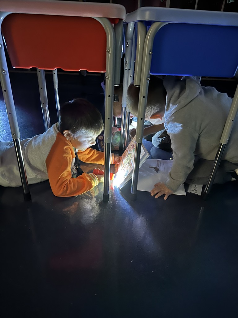 two students under desks reading with flashlights