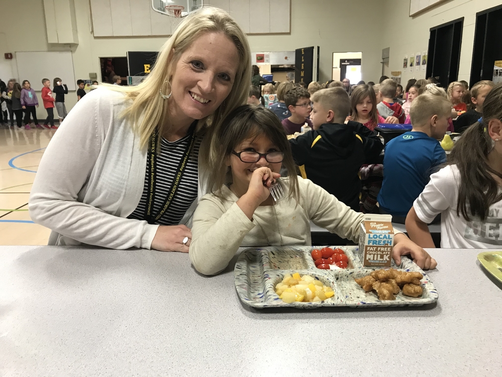Staff member sitting at a lunch table with a student smiling; student has a lunch tray with food in front of her