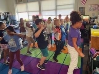 students standing on carpet in classroom watching SMARTBoard with author Jack Hartman