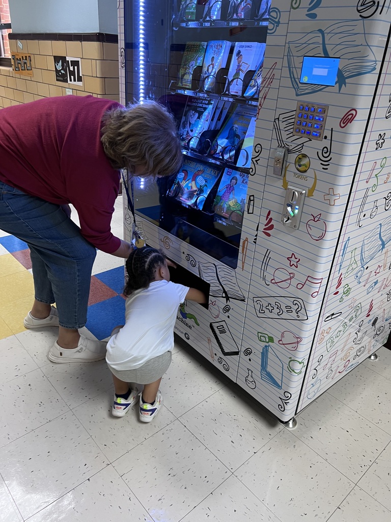 A preschooler bends down with her teacher to pick up her book.