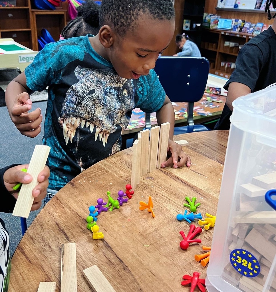 A kindergarten student lines up blocks and people to make a bridge.
