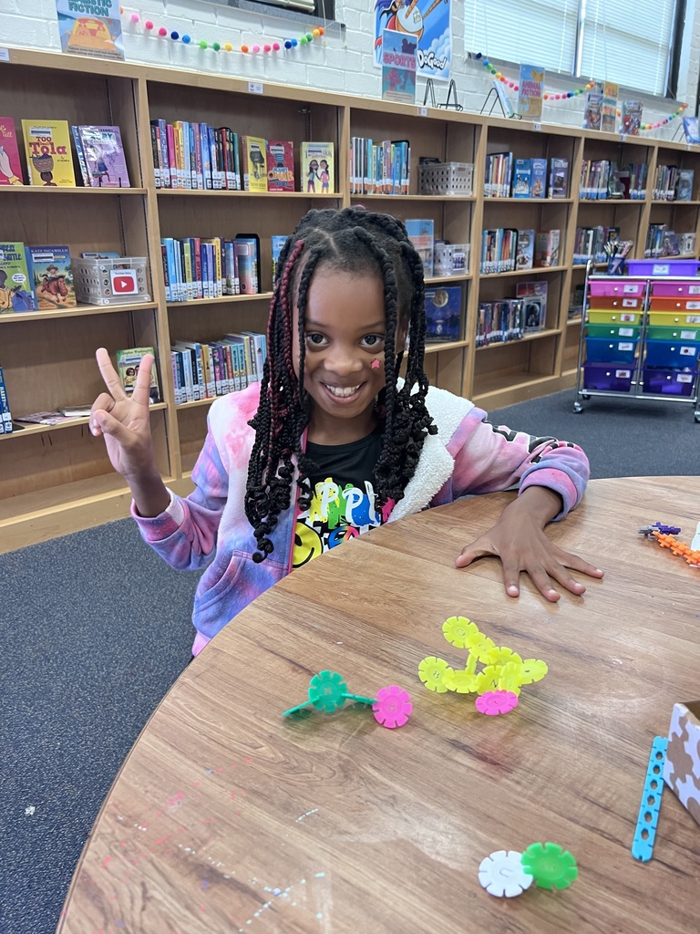 One student makes a peace sign while showing off fractions made with colorful blocks.