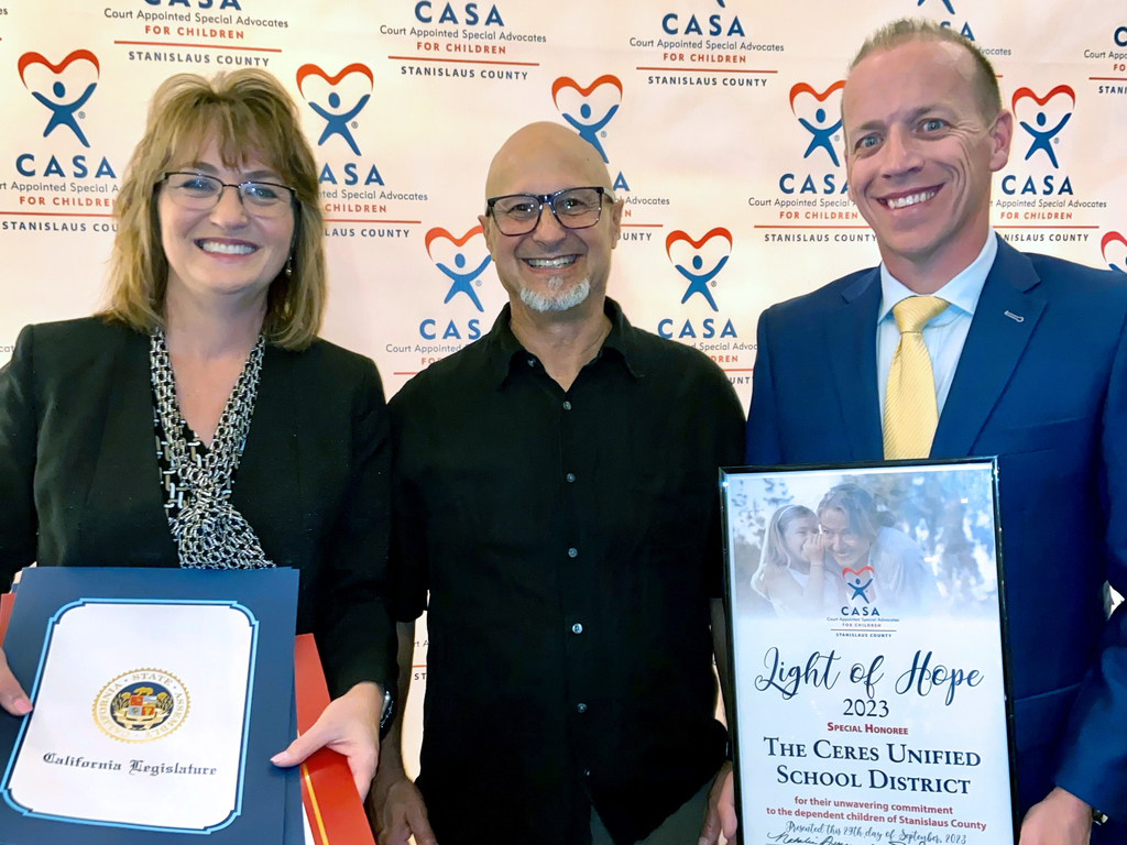 Superintendent and Board member, with presenter, hold certificates, framed picture.