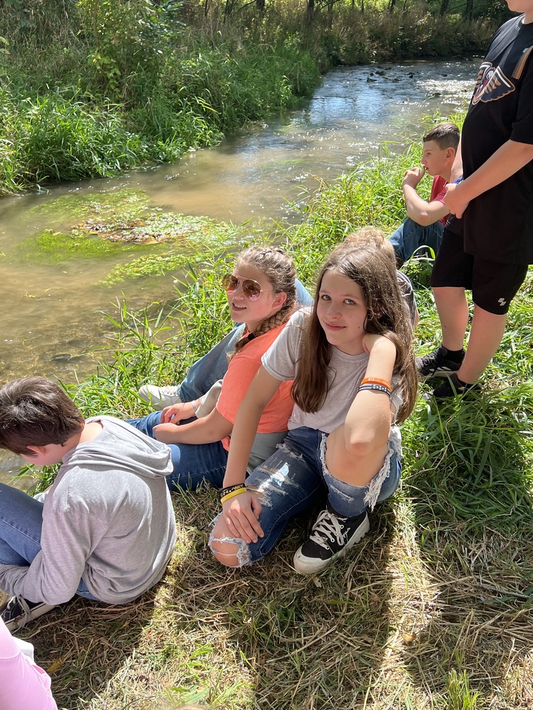 Students sit on a creek bank.