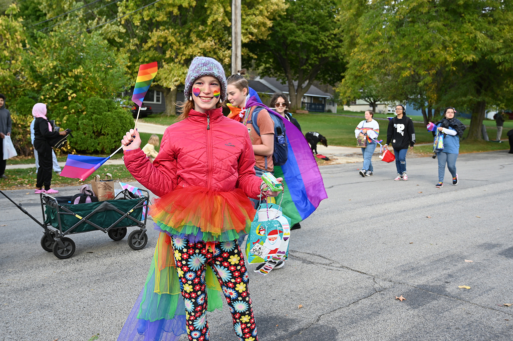 A student holding a pride flag and dressed in a colorful outfit