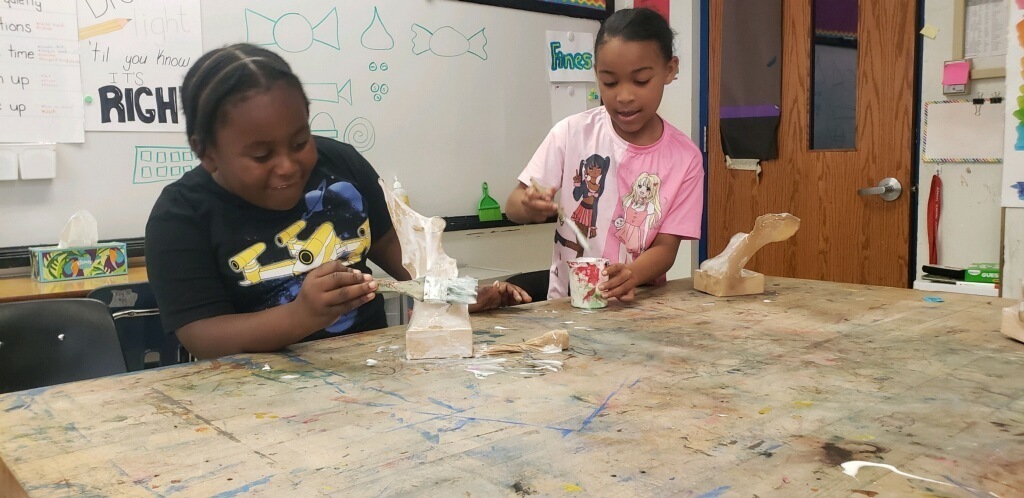 Two students paint glue on their sculptures.