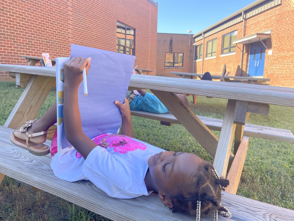 Student draws on a piece of paper while laying on a picnic bench.