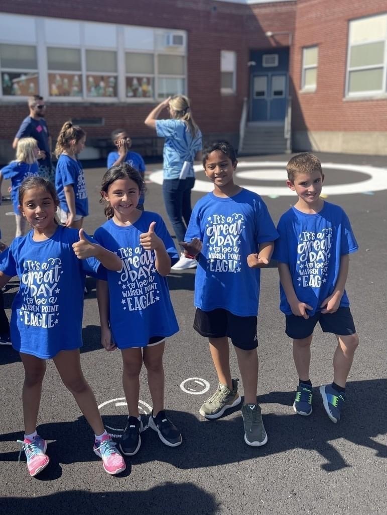 4 students wearing blue shirts with thumbs up on school blacktop