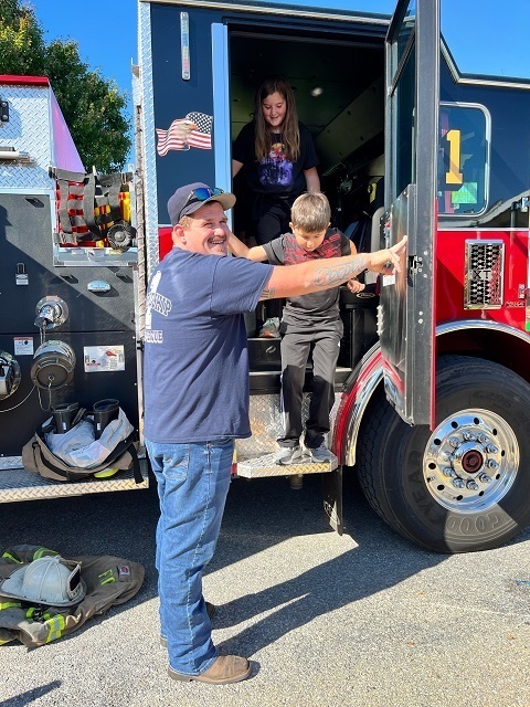 EMS worker smiling while helping male student off fire truck