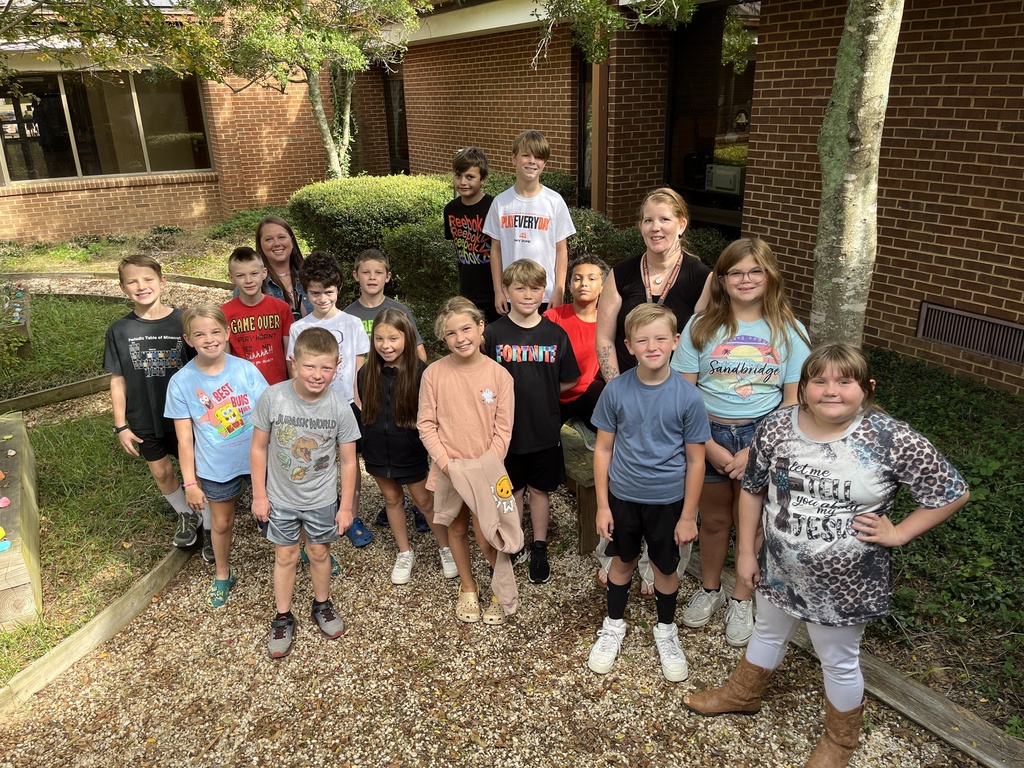 Two adults and a large group of children smile at the camera.
