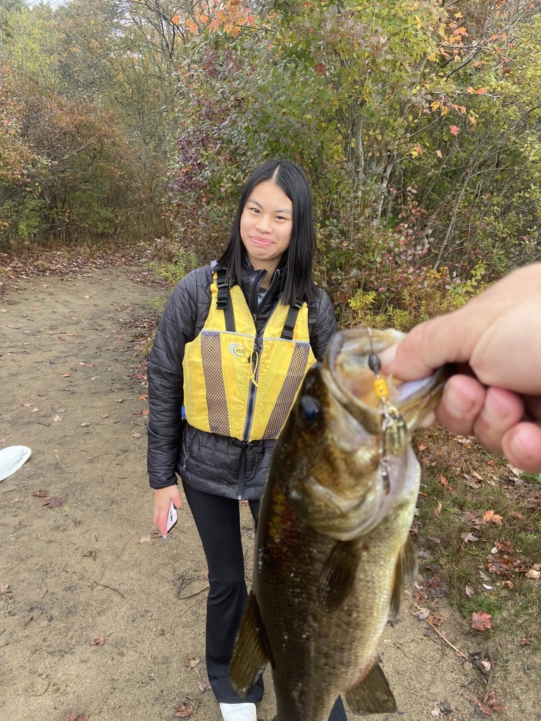 Student in black clothes with a yellow life jacket stands in the background with a hand holding a fish in the foreground