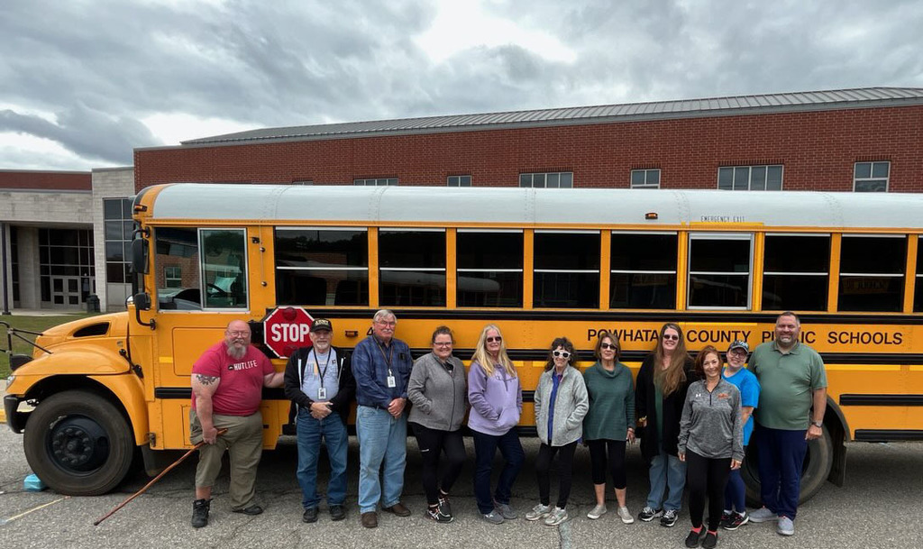 A large group of people stands in front of a school bus.