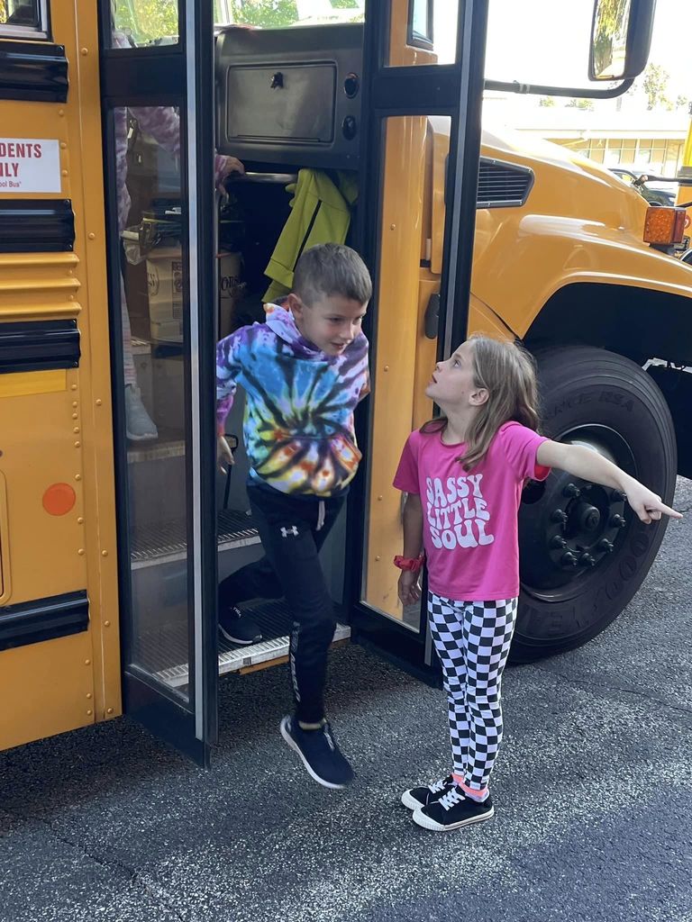 Student exiting bus with female student pointing away from the bus