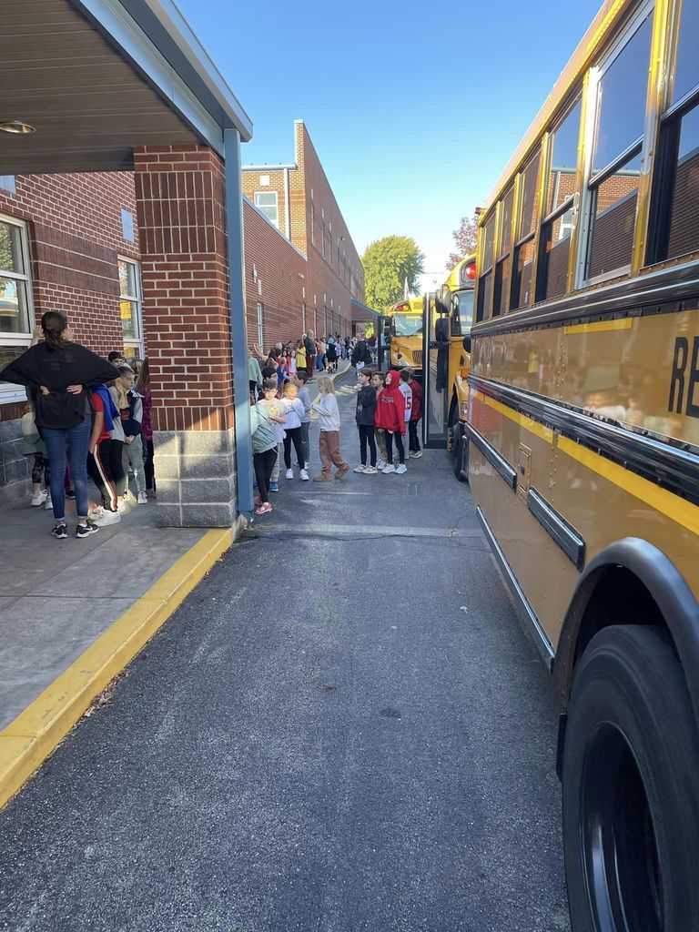 Buses lined up outside of school and students in a line next to it