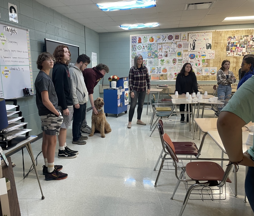 Six individuals, standing in a line. One of them is bending down and petting a dog.