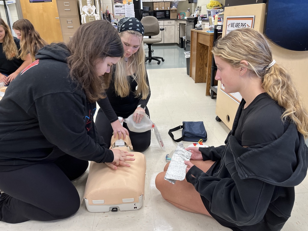 Three students learn to administer CPR.