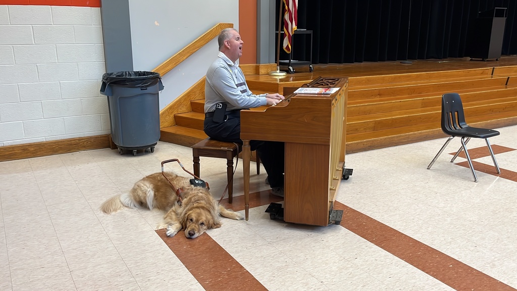 A man with a seeing eye dog sings to a group of children.
