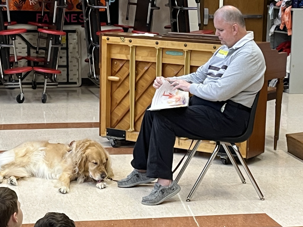 A man with a seeing eye dog reads to a group of children.