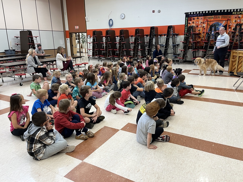 A man with a seeing eye dog talks to a group of children.
