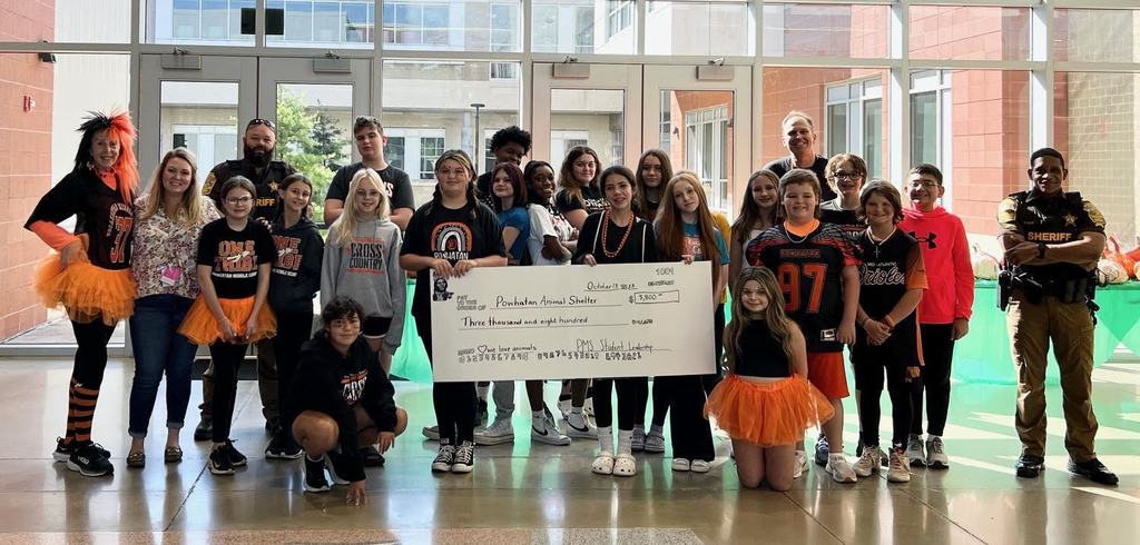 A group of students and adultts pose together holding a large check.