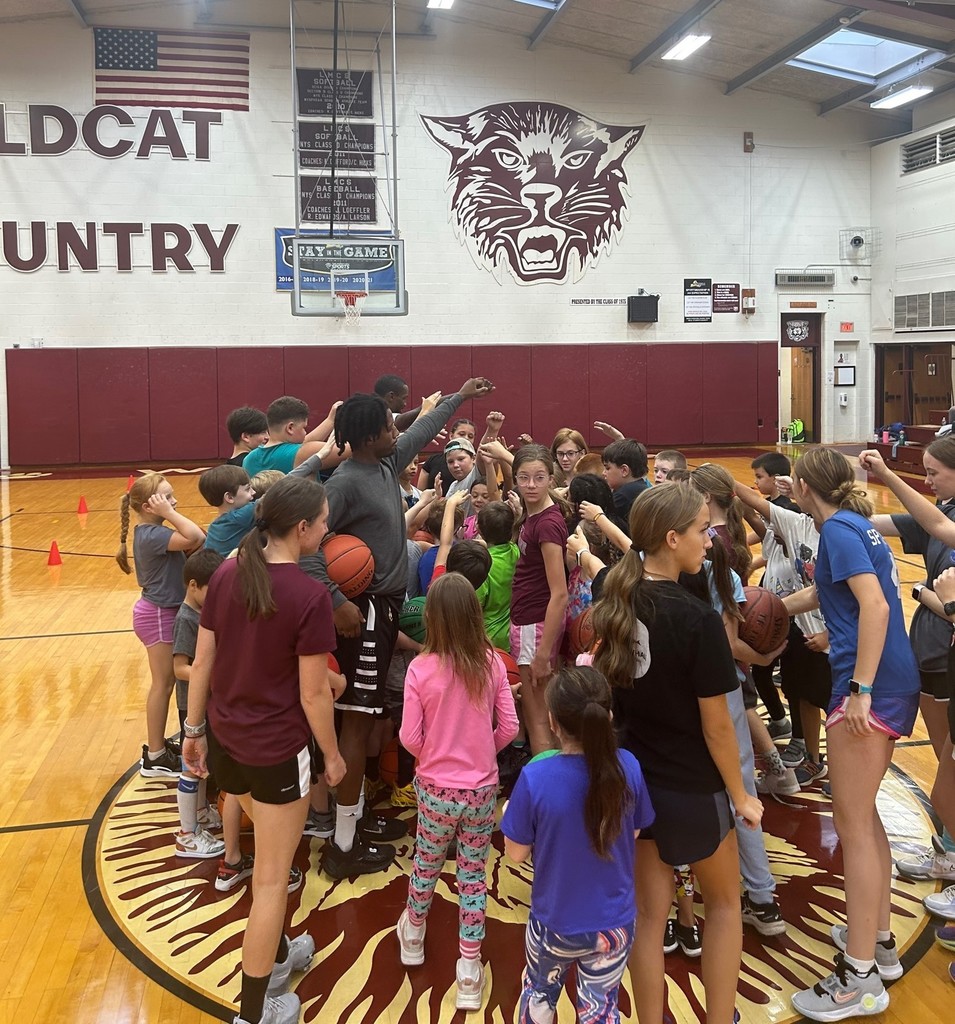 Studnets tather around a basketball player with hands toward the center