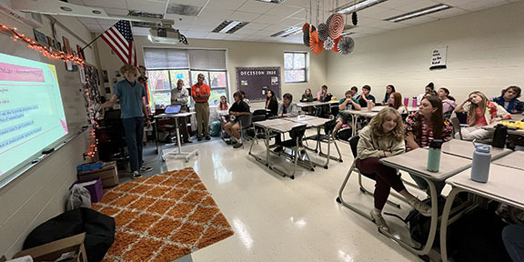 A boy speaks during a presentation. to a room full of people.