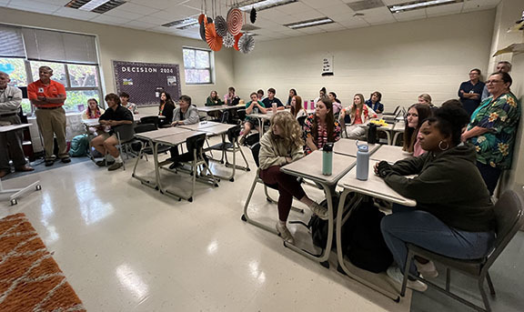 A room full of people listens to a speaker.