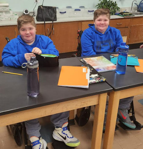 Twho students wearing blue hoodies sit at desks