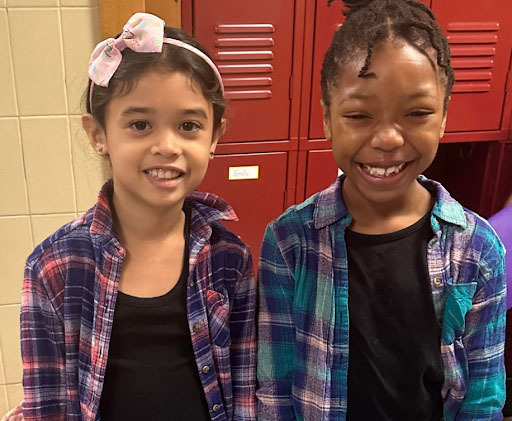 Two students wearing black shirts and purple, pink and blue flannels smile 