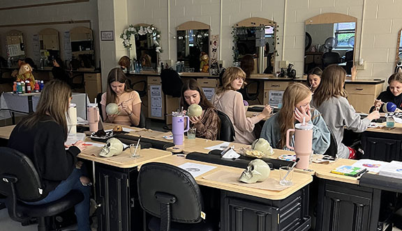 Students decorate and label skulls during cosmetology class.
