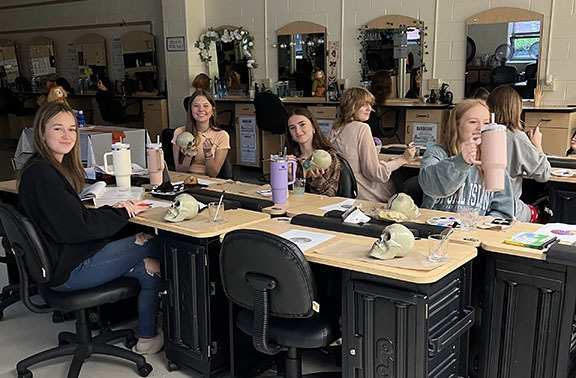 Students decorate and label skulls during cosmetology class.