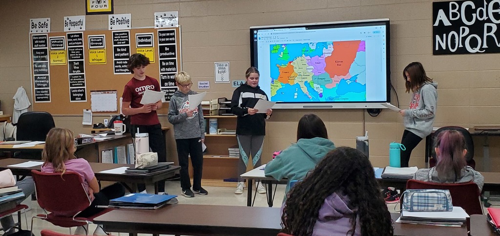 Middle school students standing at the front of the room making a presentation. There is a map on the board behind them.