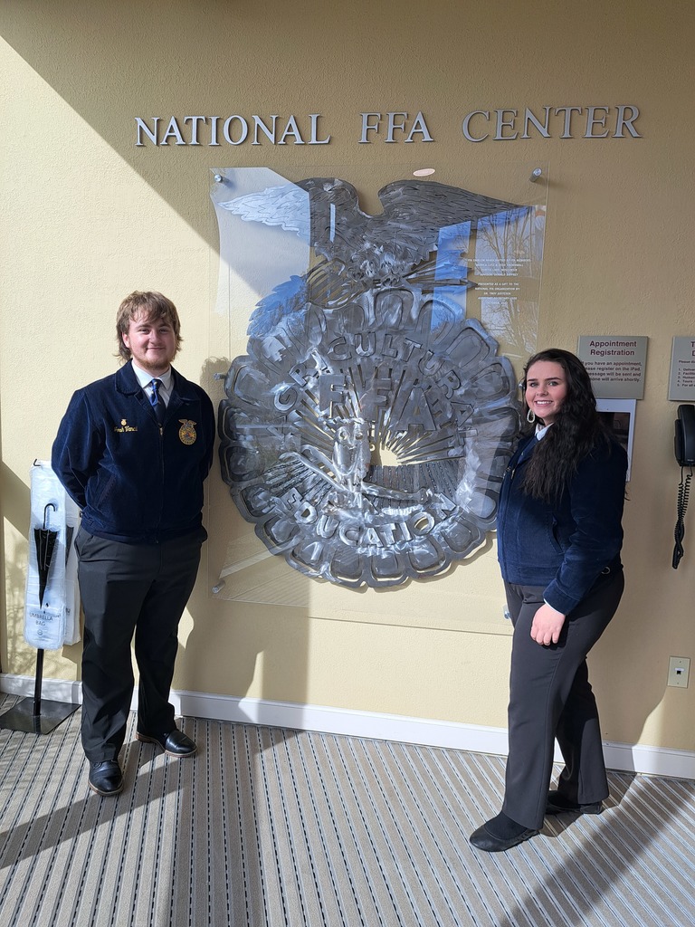 2 students standing next to a large national FFA symbol