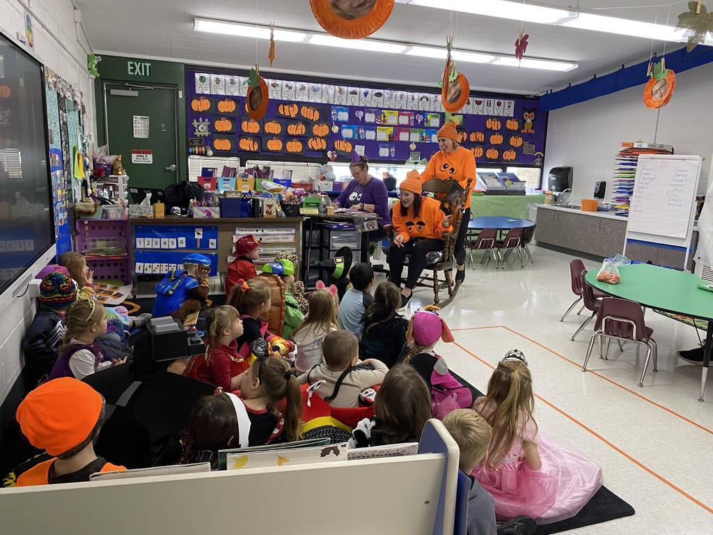 A teacher, seated in a chair, reading to students seated on a carpet listening.