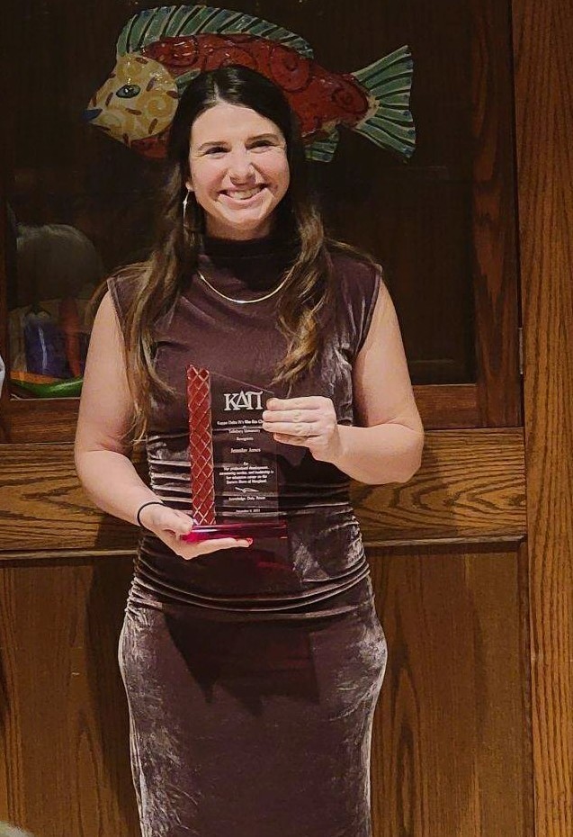 woman in a brown dress smiling holding an award