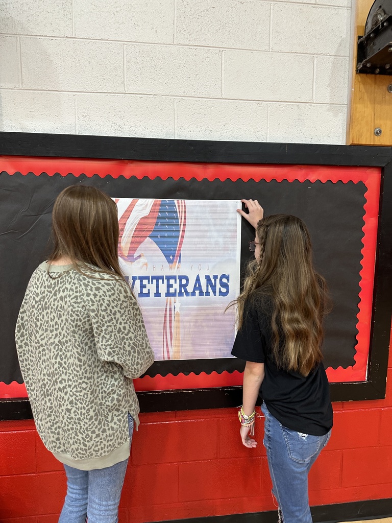 Two girls hang a sign the says "Thank You Veterans."