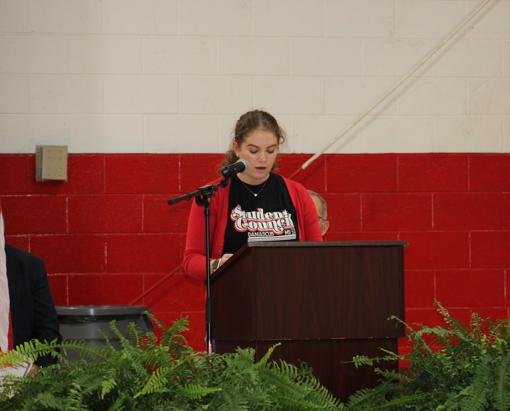 A girl reads at a lectern in a gym.