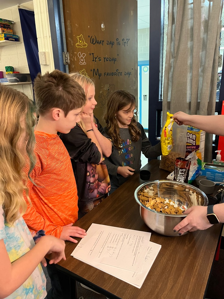 students measuring ingredients to pour into a bowl of trail mix 