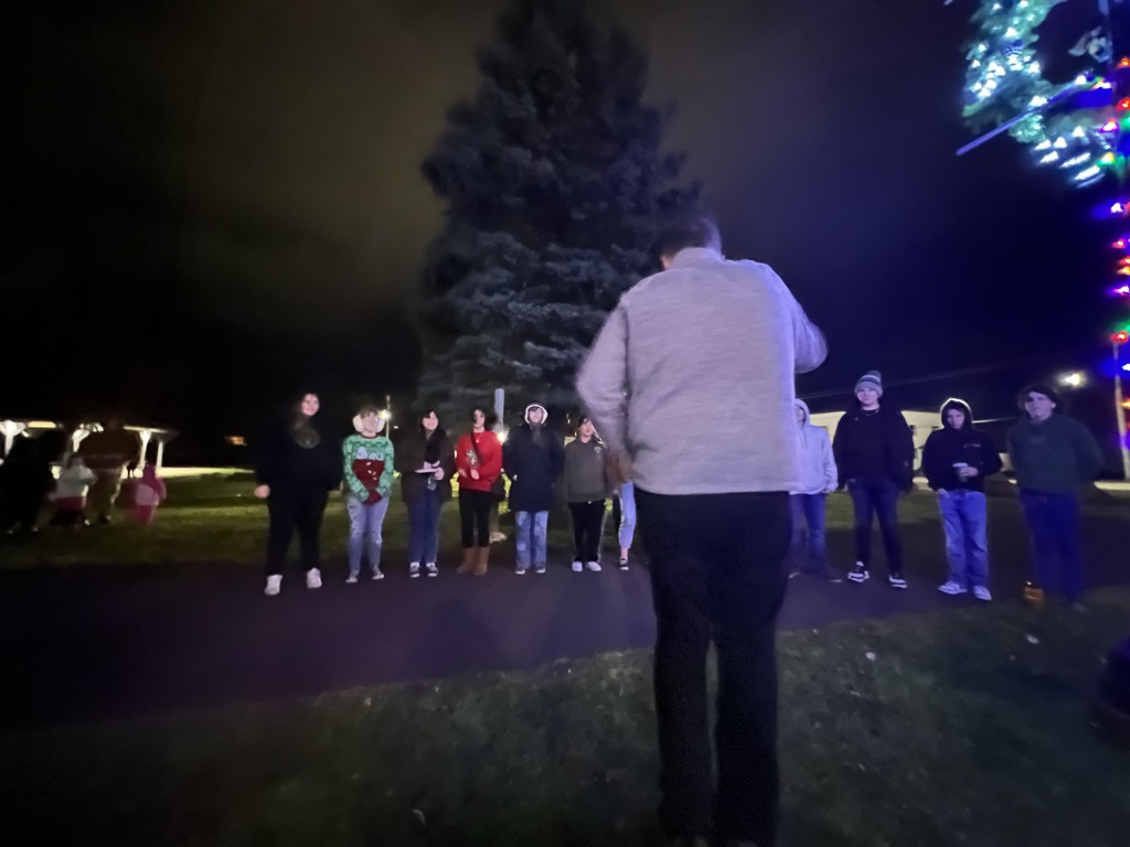 A person conducts a group of students in front of a tree