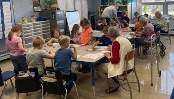 students and elderly seated at tables working on an art project