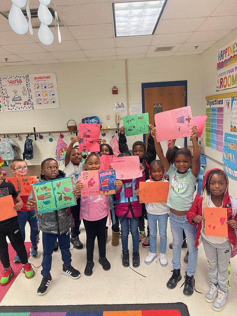 First graders hold up their letters on colored paper.